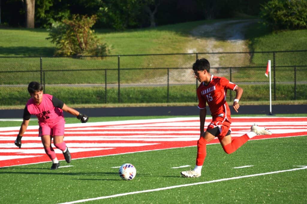 Young soccer player dribbling past goalkeeper on field.