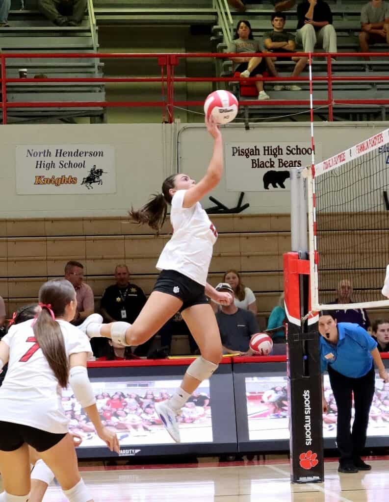 Female volleyball player jumping to hit the ball during match at high school gym.