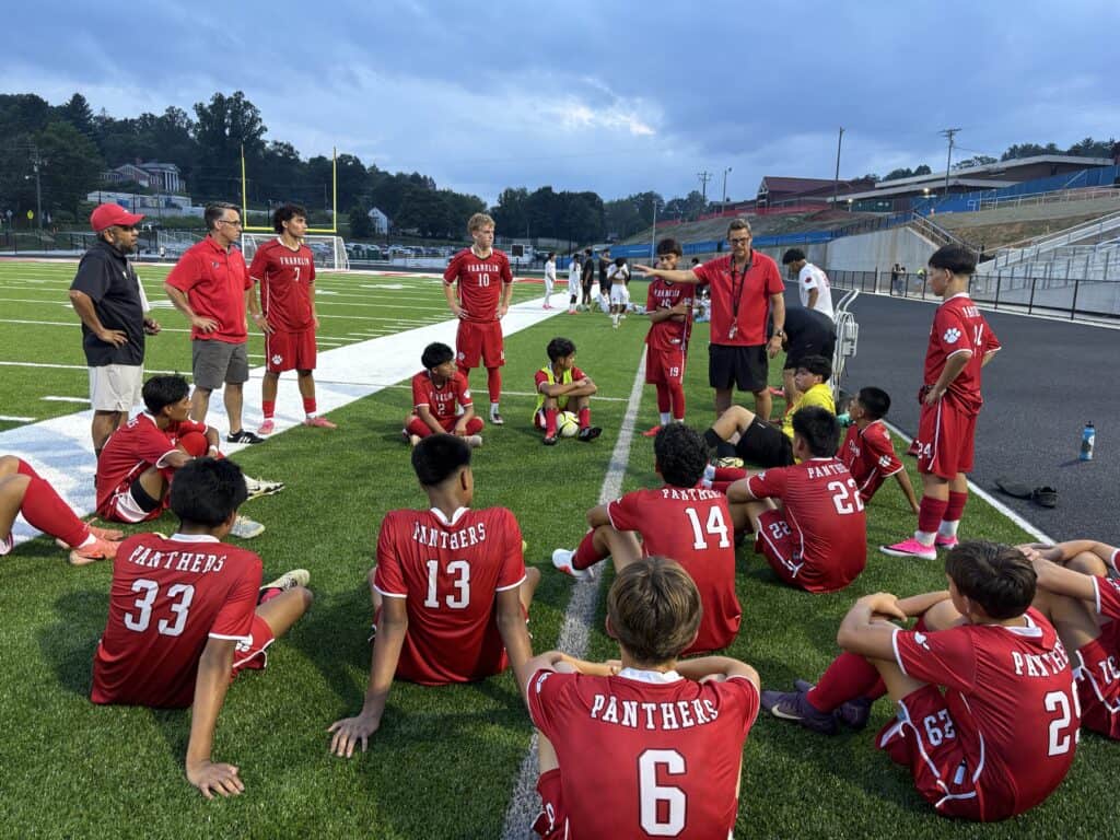 FHS men's soccer team listening to coach during pre-game talk on the field.