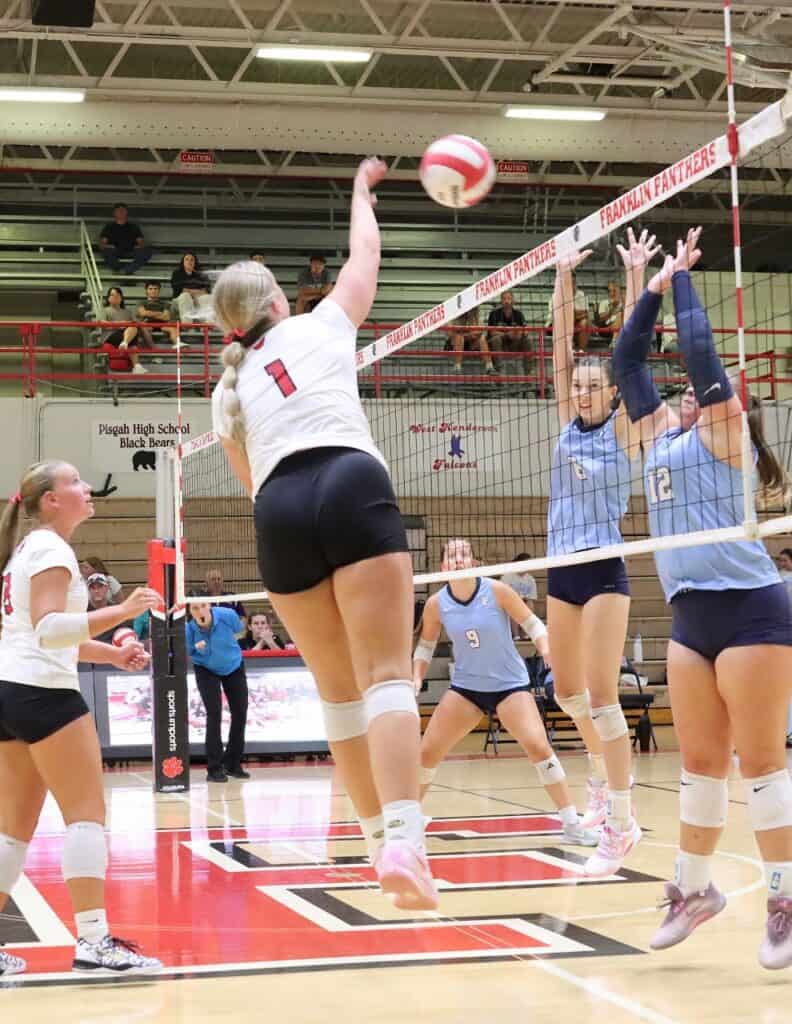 High school volleyball game with players jumping for the ball.