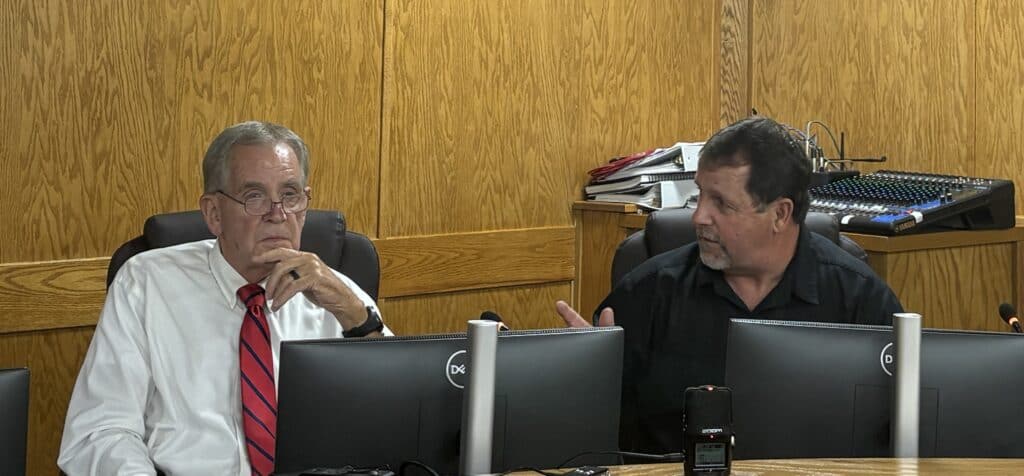 Two men in a business discussion at a desk with computers.