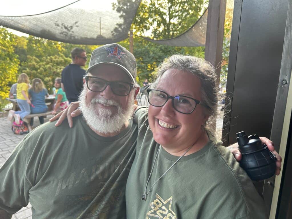 Two smiling veterans at Macon Sense event with outdoor setting and other attendees in background.