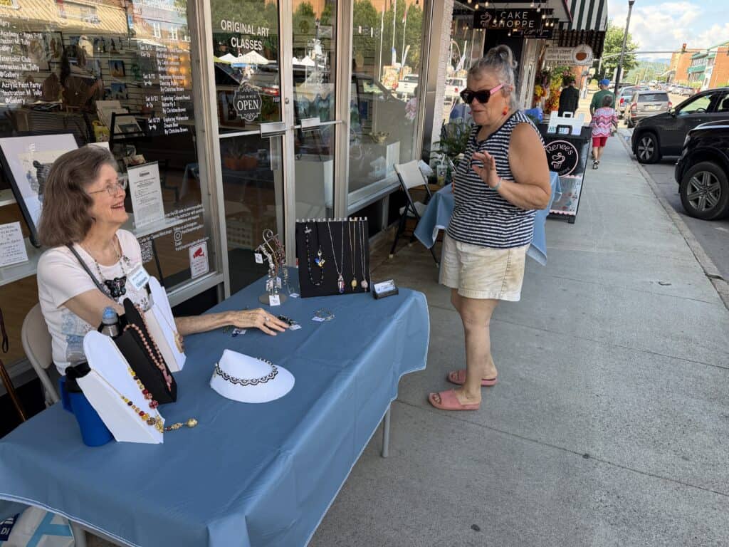 Woman shopping jewelry at Macon Sense art festival on downtown sidewalk.