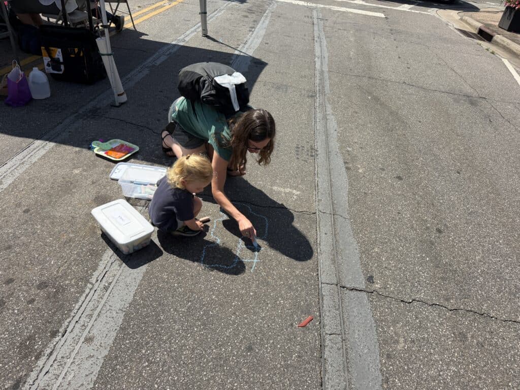 People creating sidewalk art during a community event in an urban area.