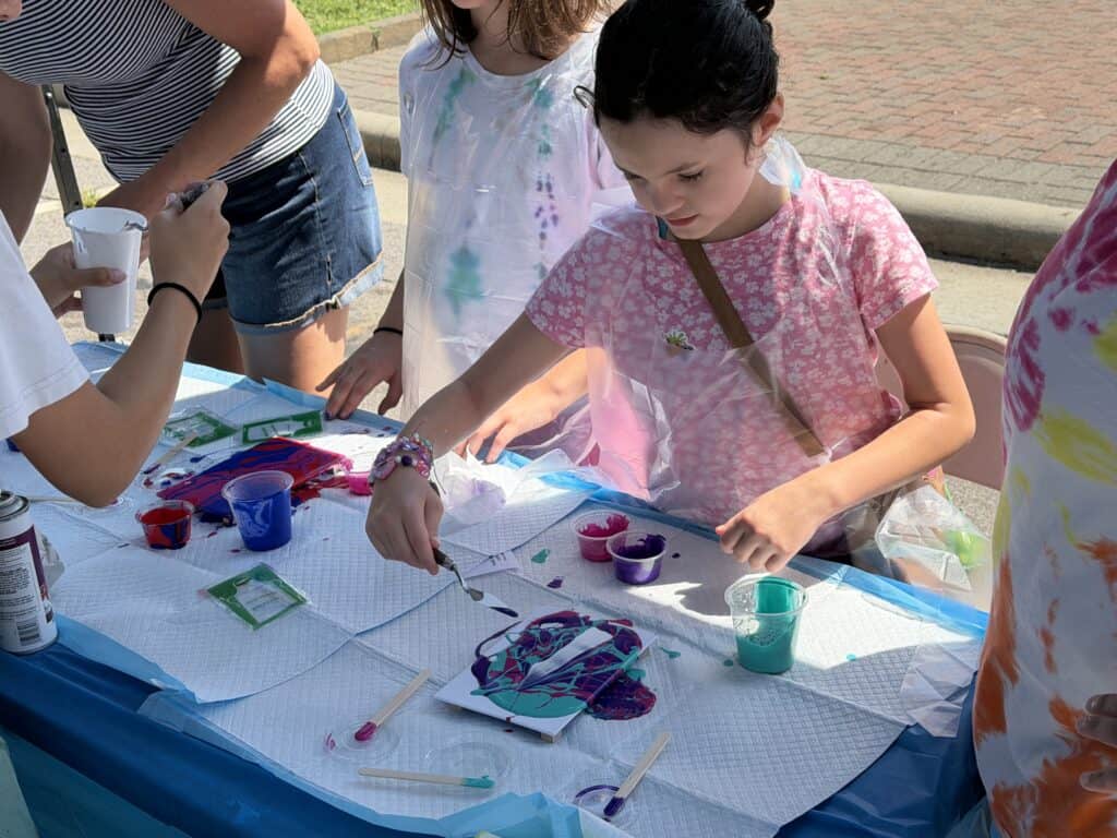 Young girl painting with colorful paints at outdoor art activity.