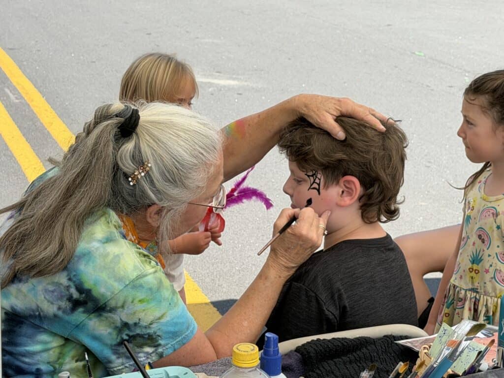Child getting face painted at Macon Sense event with colorful designs.