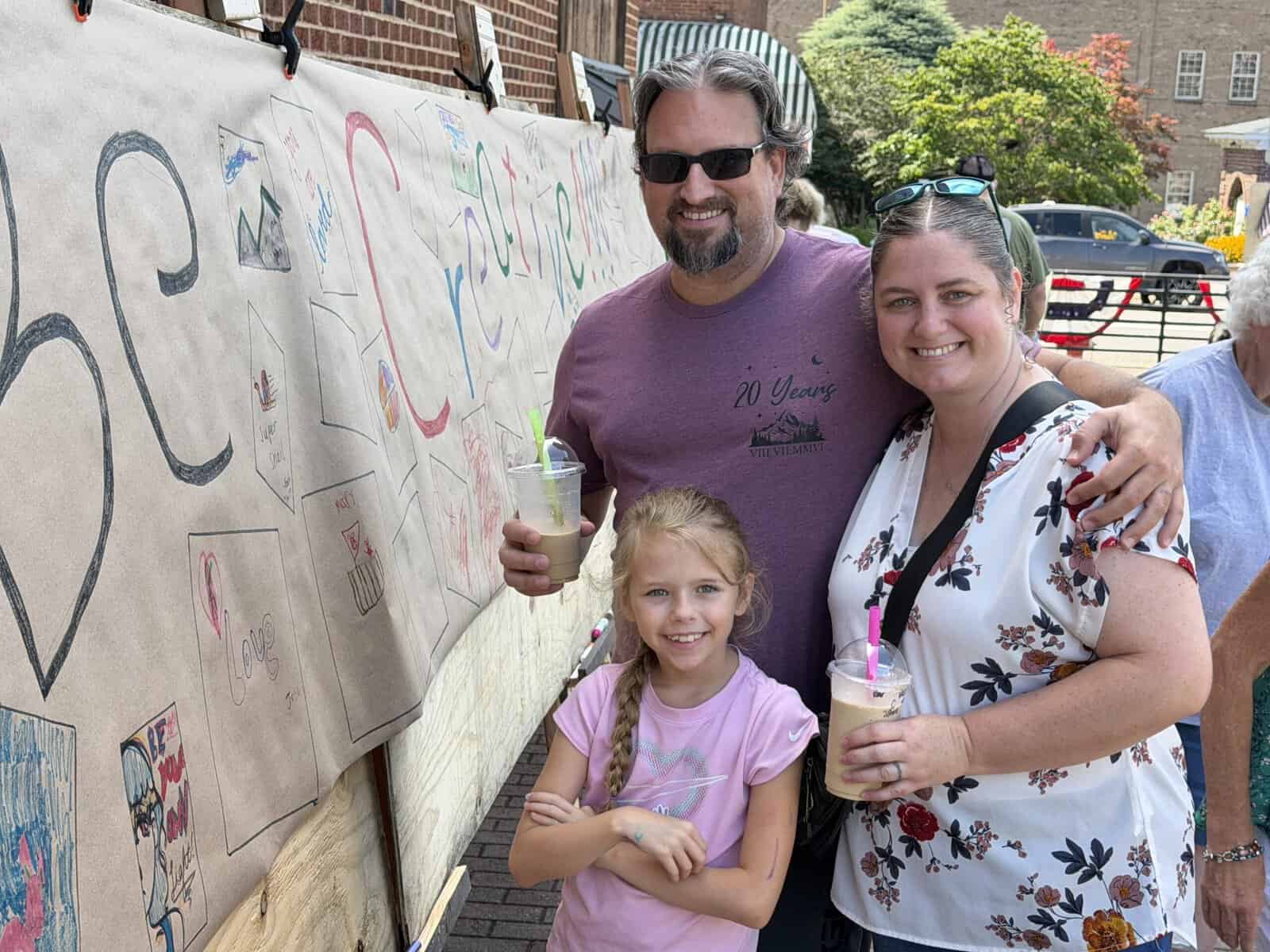 Family with two children smiling and holding ice cream cones outdoors.