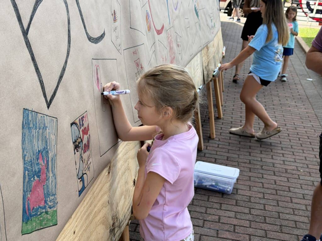 Young girl drawing on outdoor wall with chalk at community event.