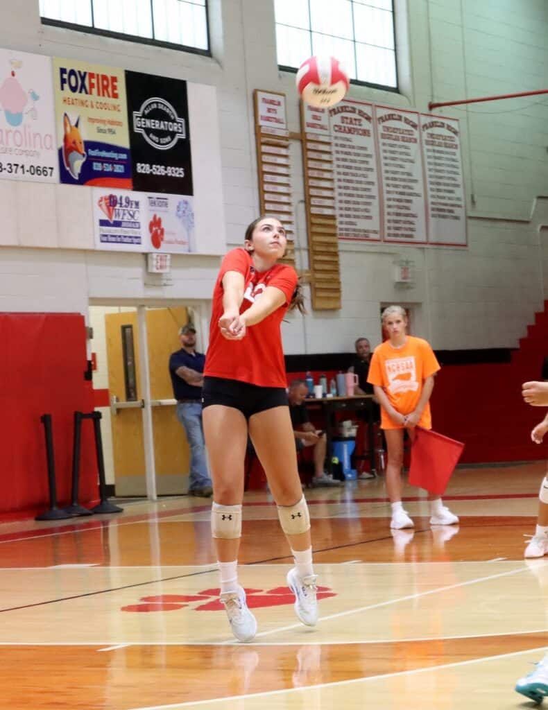 Female volleyball player serving the ball during a match at the gym.