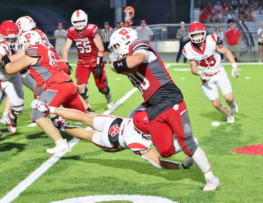 Football player running with ball as opponents try to tackle him.
