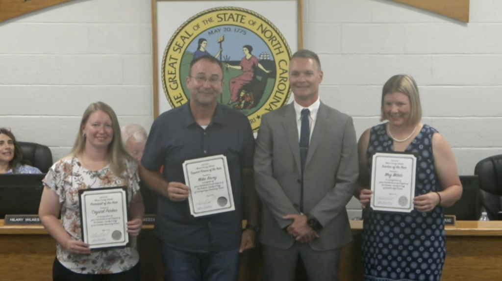 School officials holding safety awards in front of North Carolina seal.