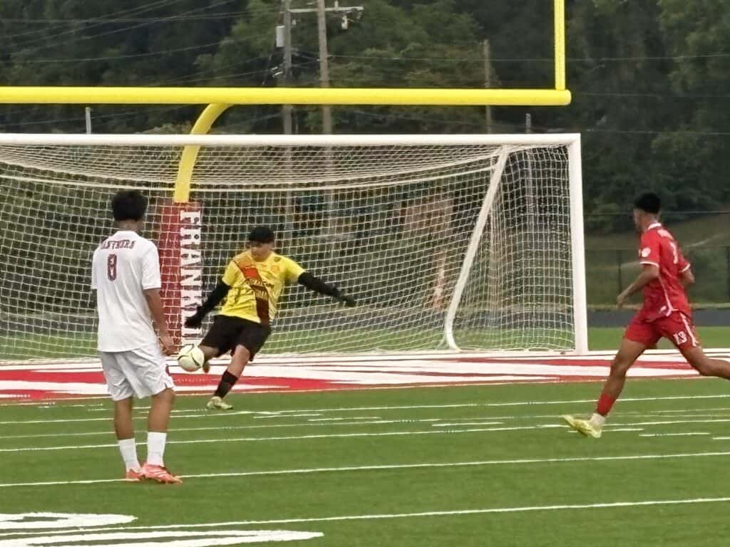 FHS men's soccer player kicking ball towards goal during match.