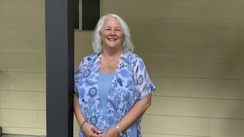 Smiling elderly woman with white hair in blue floral top outside.