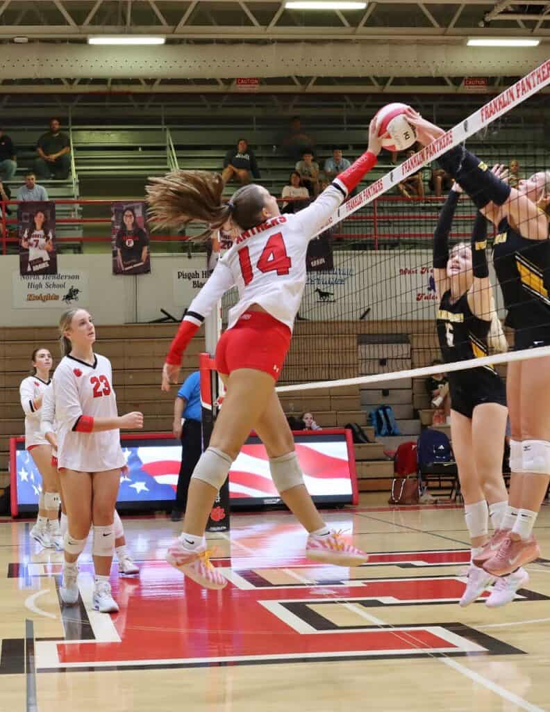 Female volleyball player in mid-air spike during match at gym.