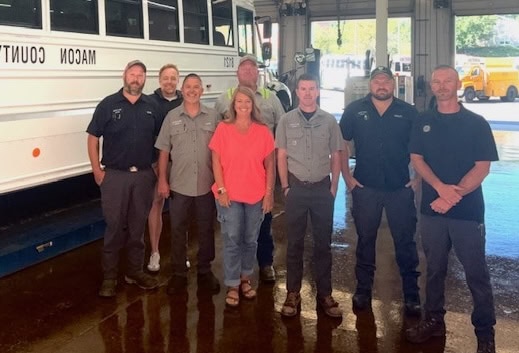 Group of staff members standing in bus service center with bus in background.