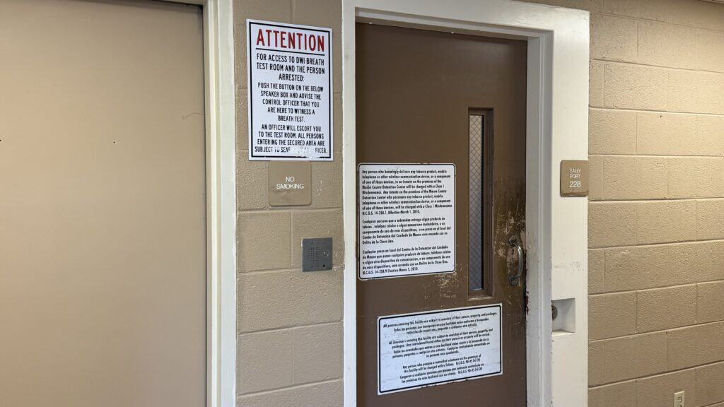 Door with multiple warning and informational signs in a beige wall.