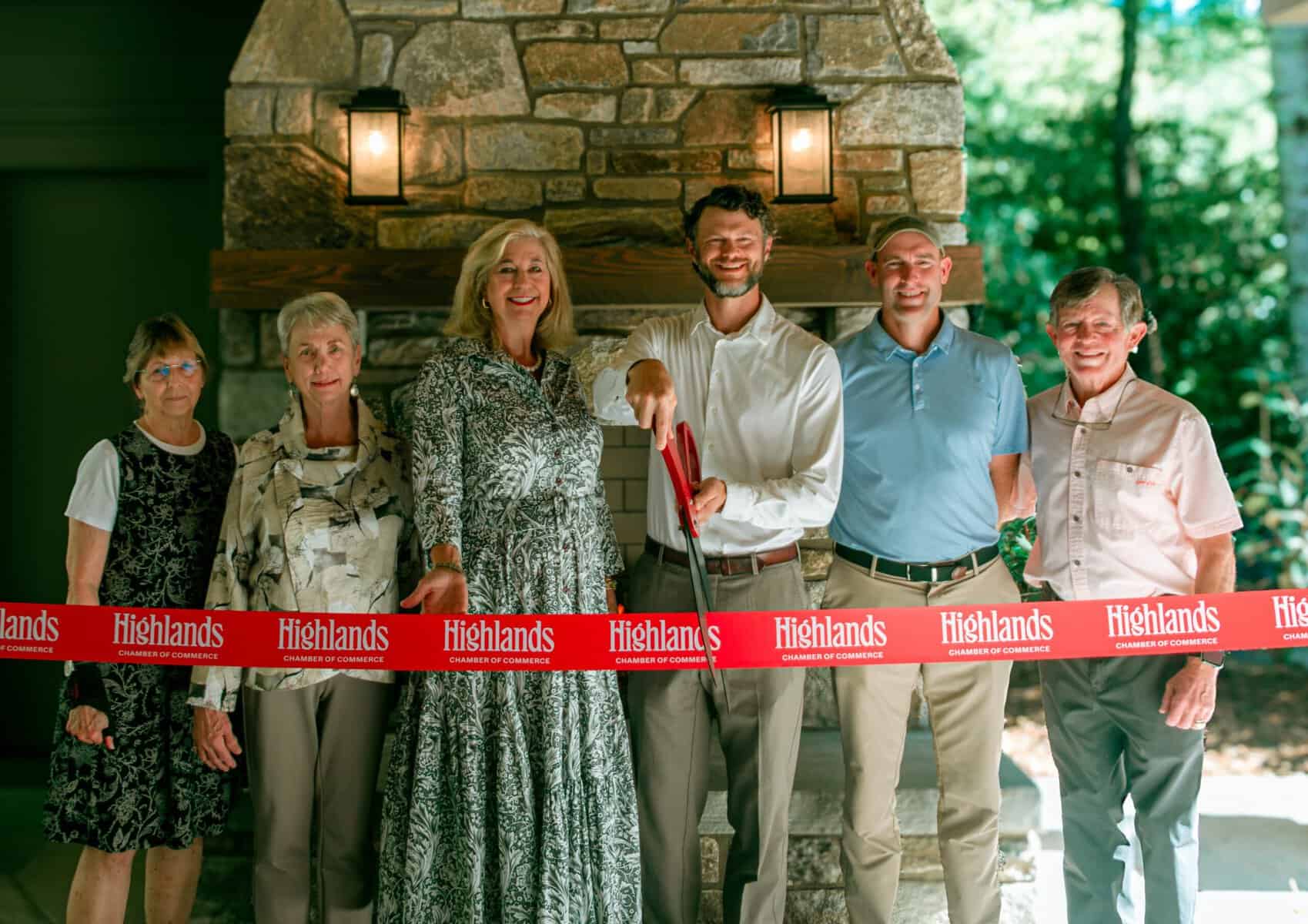 Group of diverse people at ribbon-cutting event outdoors by fireplace.