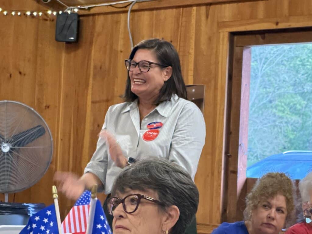 Woman smiling and clapping at campaign event with American flags.