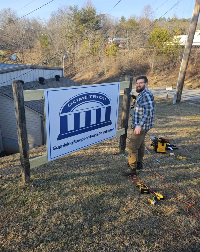 Man installing a sign for Dometrics with tools on the ground.