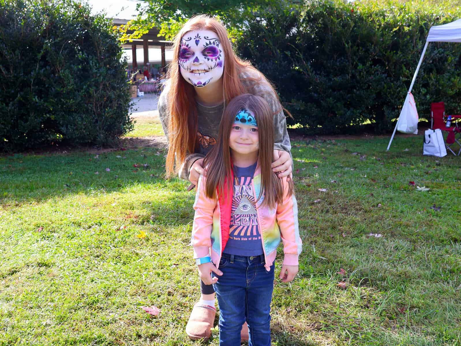 Woman and girl with face paint at Mountaineer Festival in outdoor park.