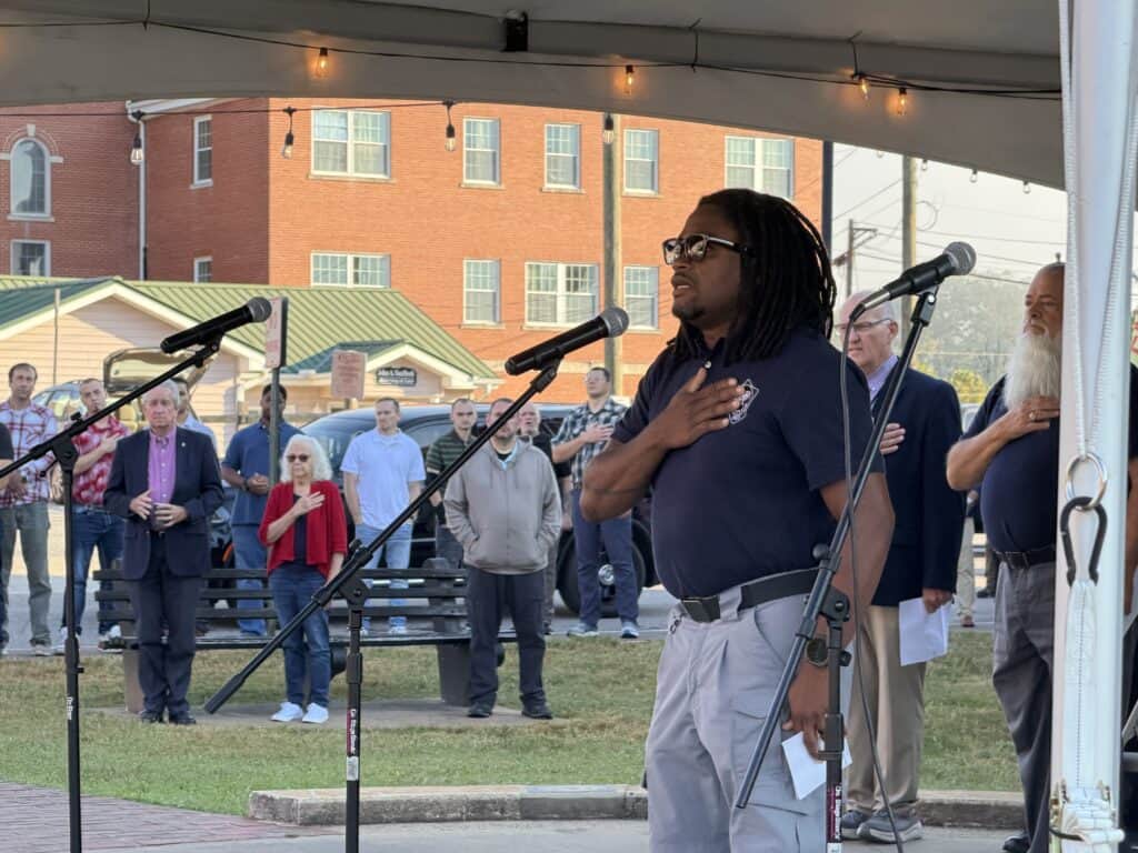 Man with dreadlocks and glasses at outdoor community event.