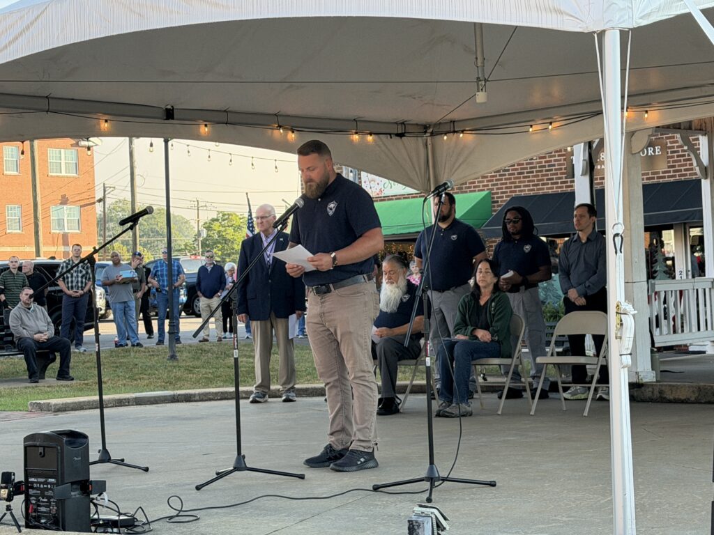 Man speaking at 9/11 remembrance event in Macon under a tent.