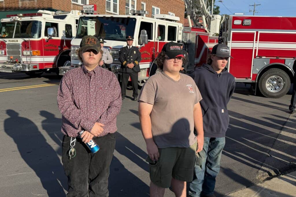 Three young people standing in front of fire trucks at a community safety event.