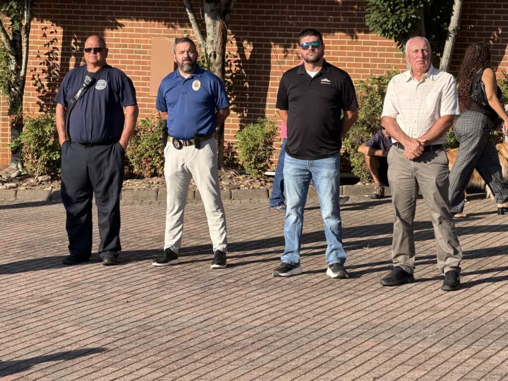 Group of four men standing outdoors at a community event.
