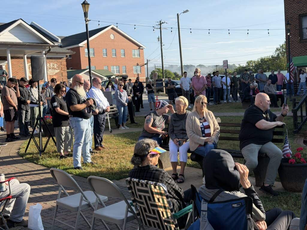Community gathering in Macon with people listening and socializing outdoors.