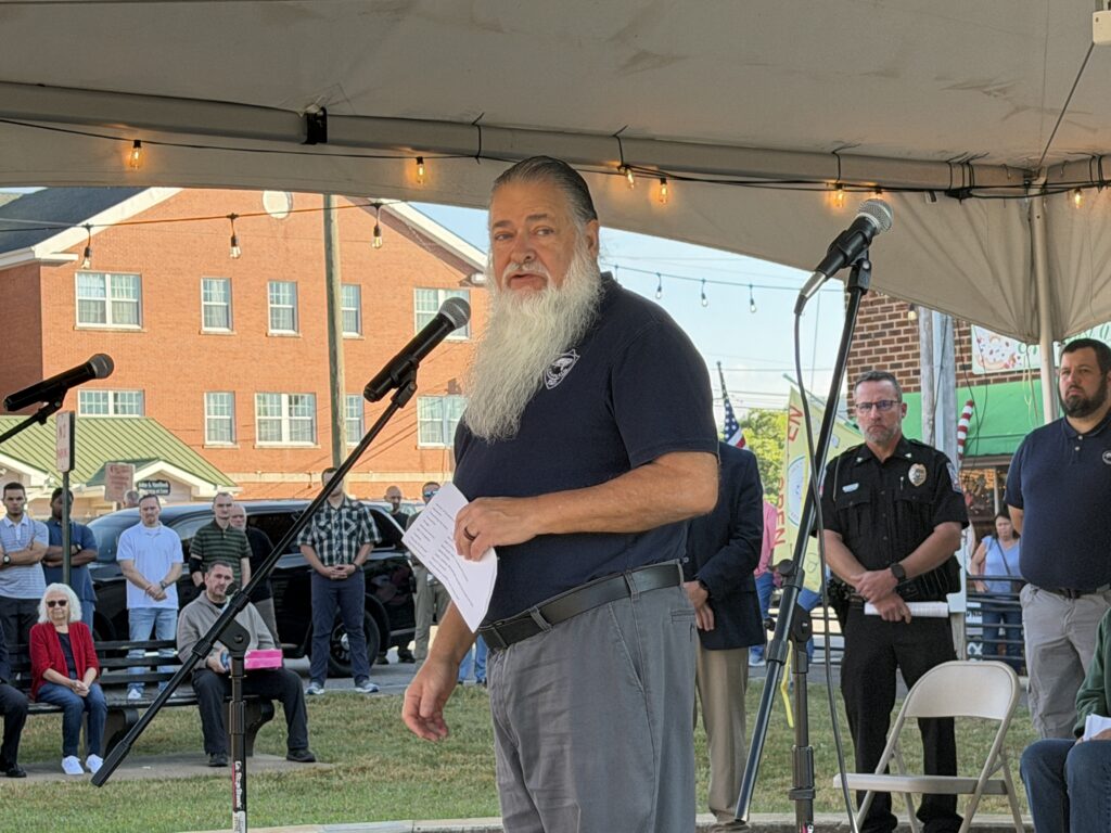 Elderly man speaking at a memorial event during Macon remembrance.