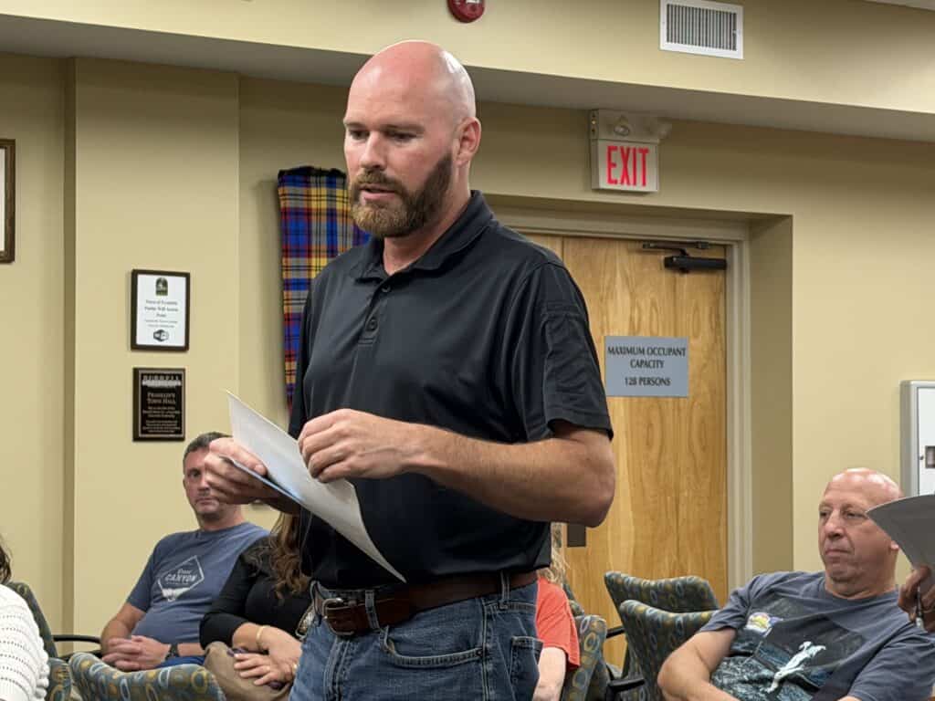 Man speaking at community meeting with attendees listening attentively.