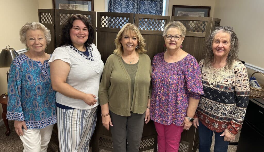 Group of five women standing together in an office environment.