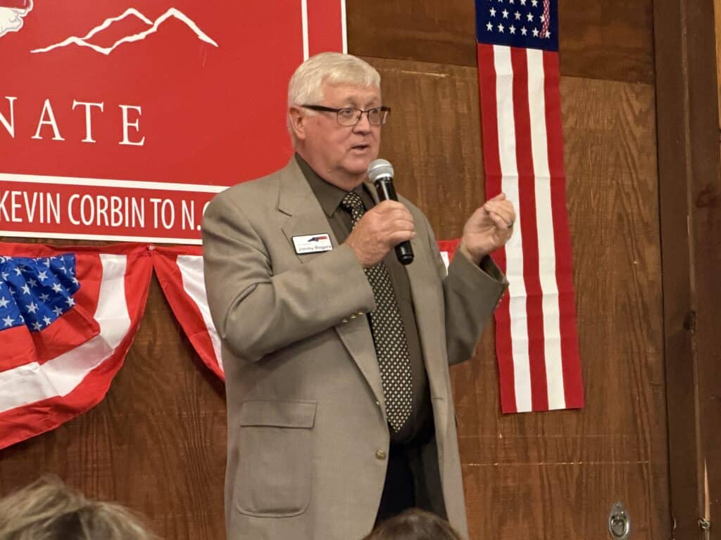 Kevin Corbin speaking at a campaign event with American flags in the background.