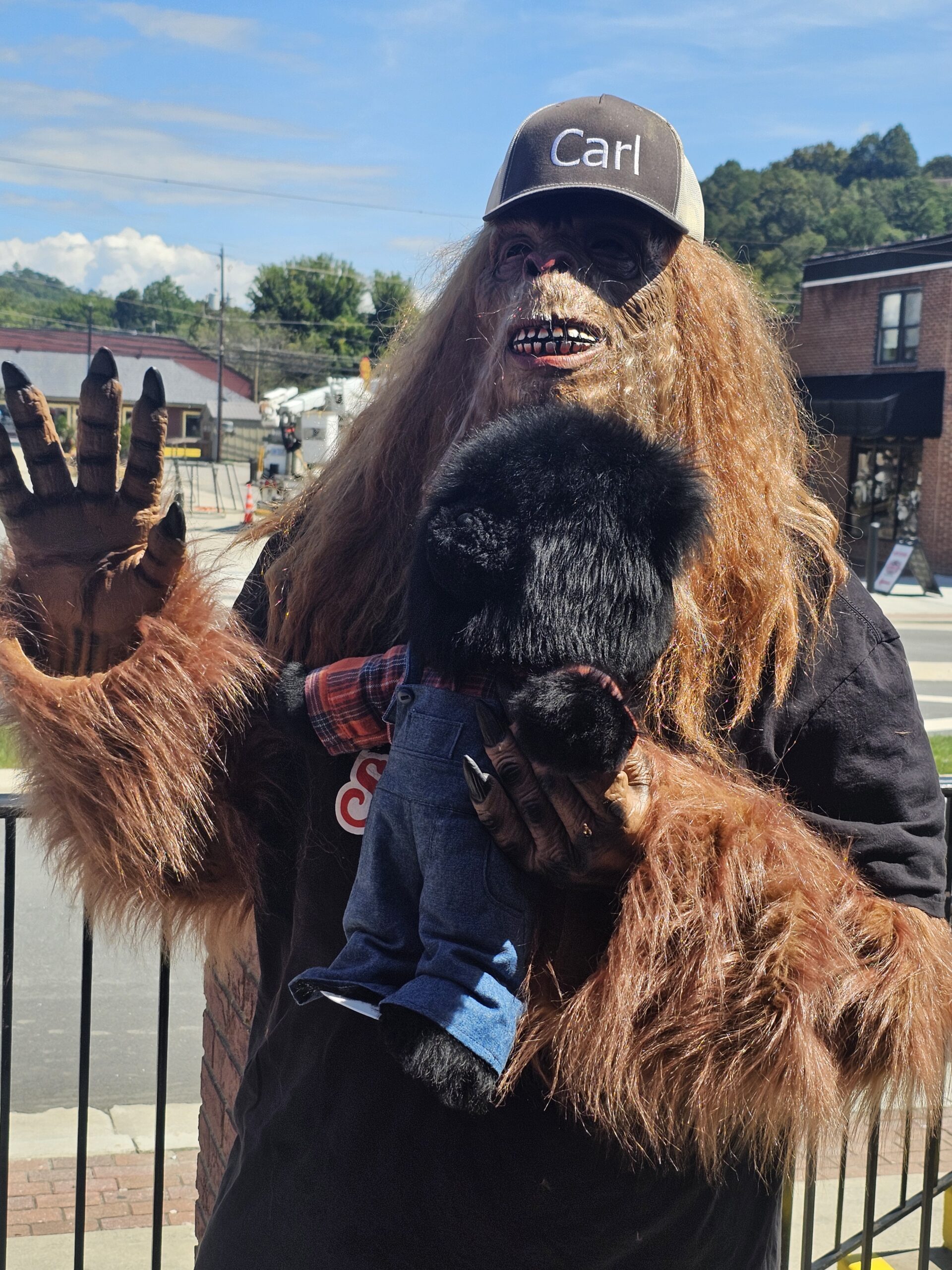 Person in Bigfoot costume with dog outdoors on sunny day.