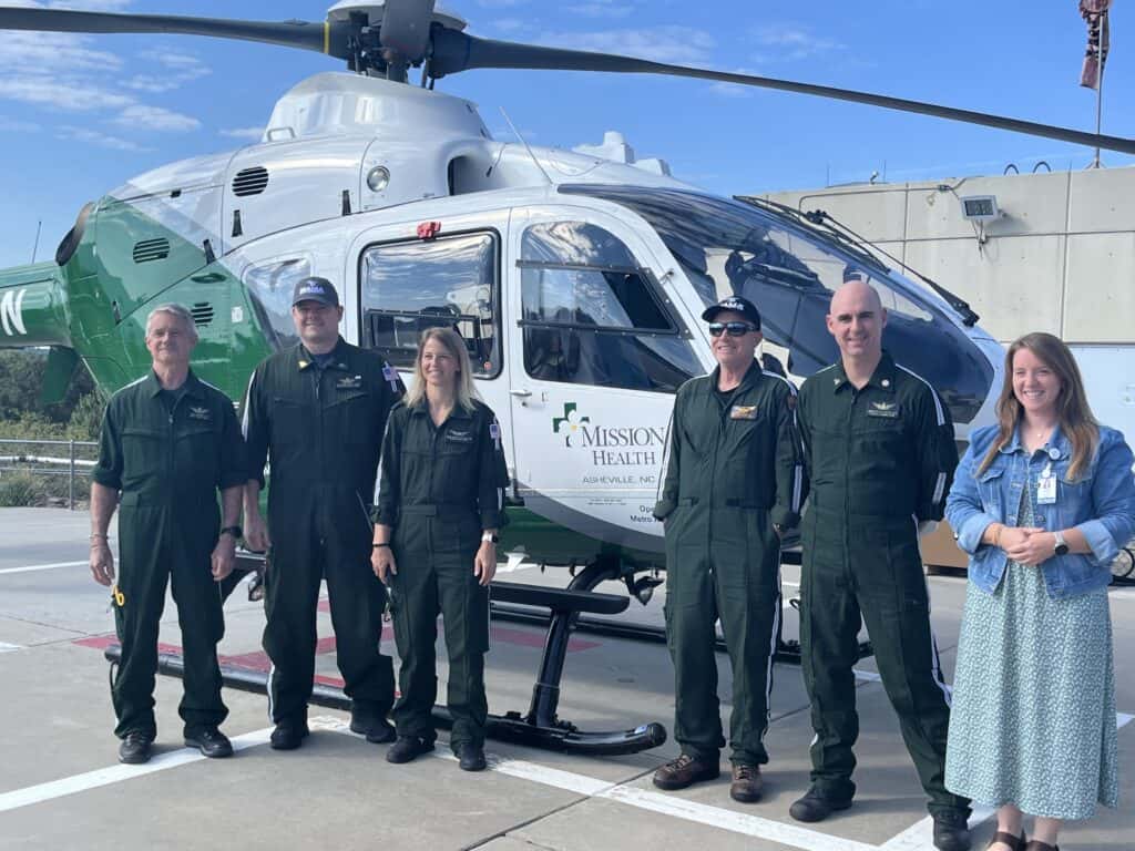 Helicopter crew members standing in front of rescue helicopter at airport.