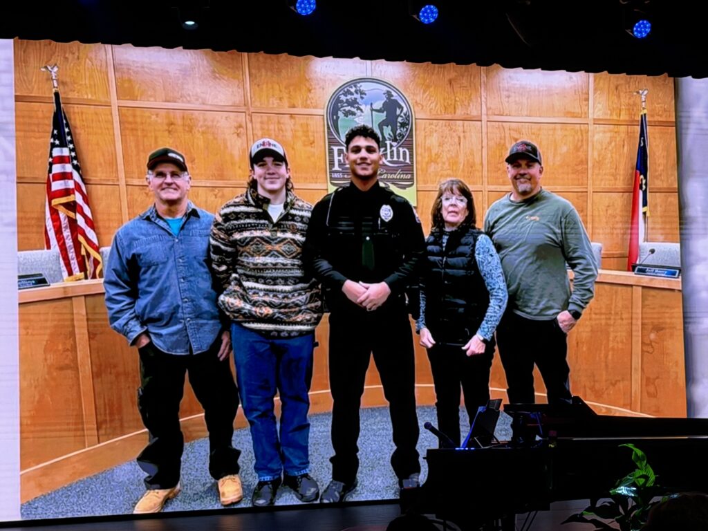 Group of five people standing in a courtroom with American flags and a wooden backdrop.