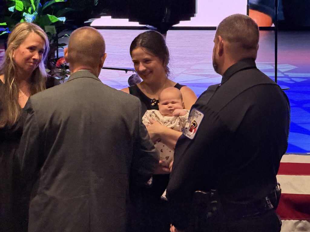 Family and police officer at a celebration event with a baby.