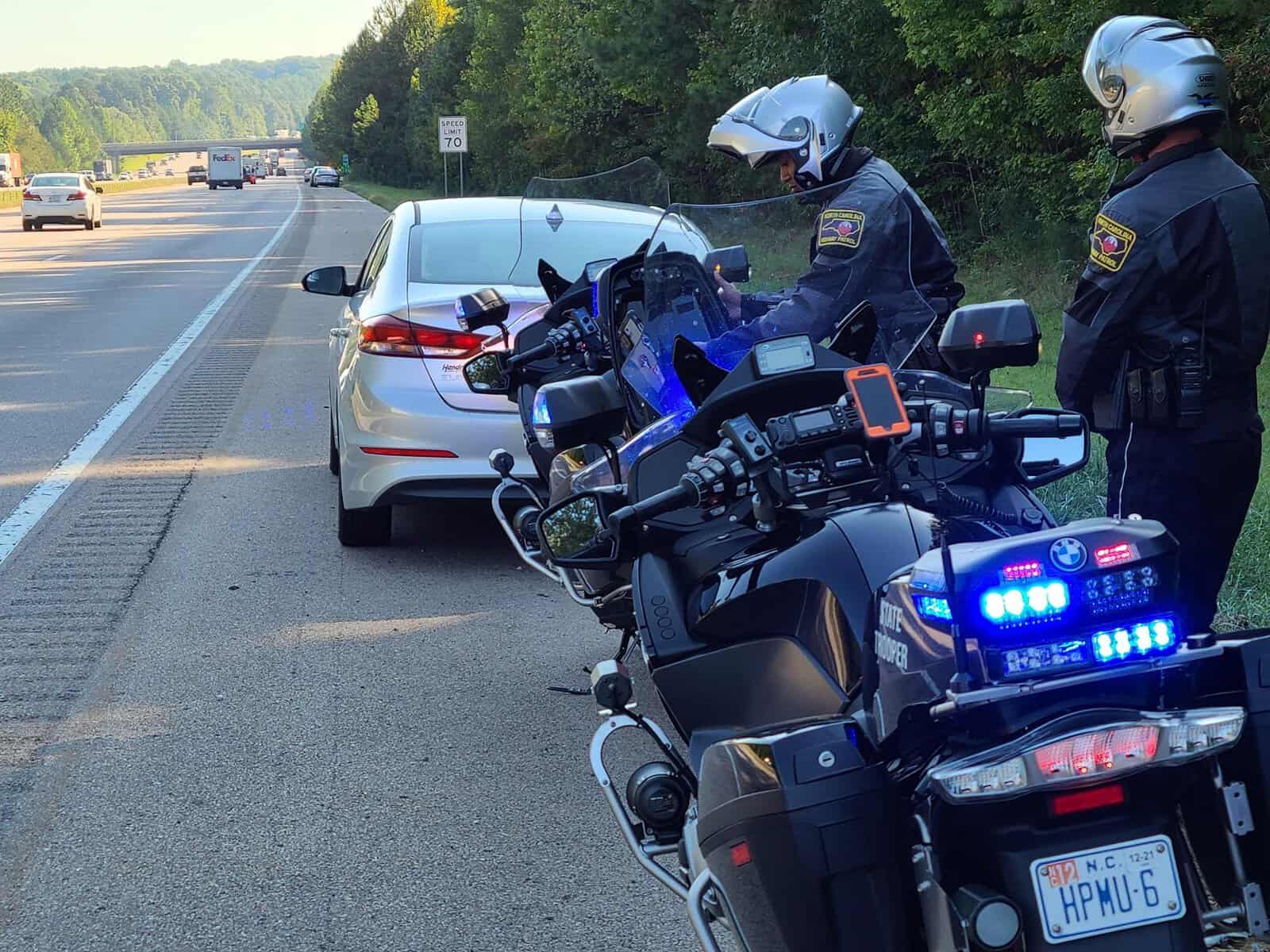 Police officers stop a white car on the highway for inspection.