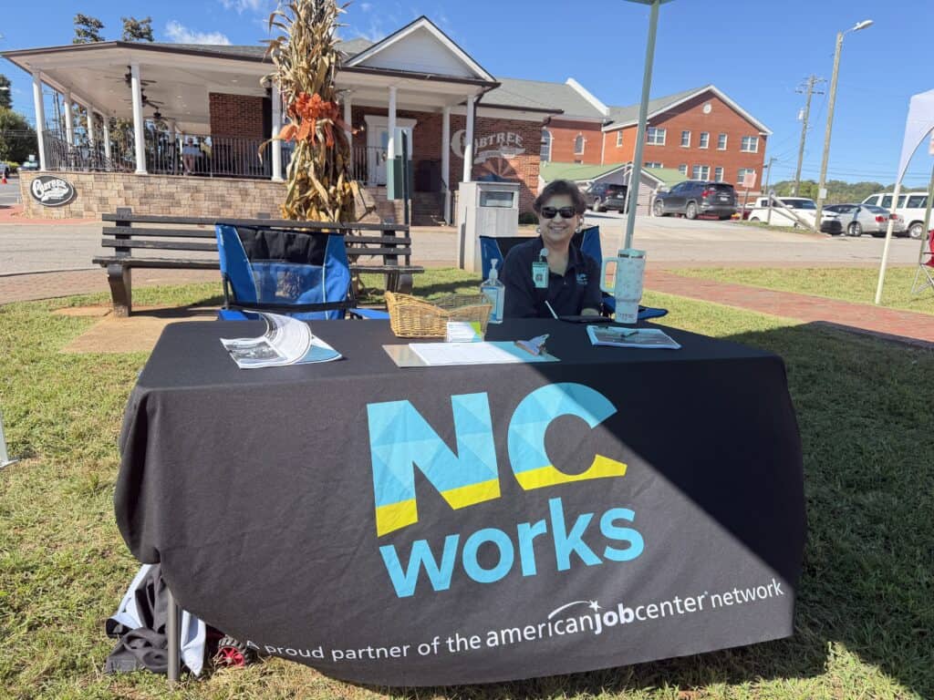 Woman at NC Works job fair booth outdoors on a sunny day.
