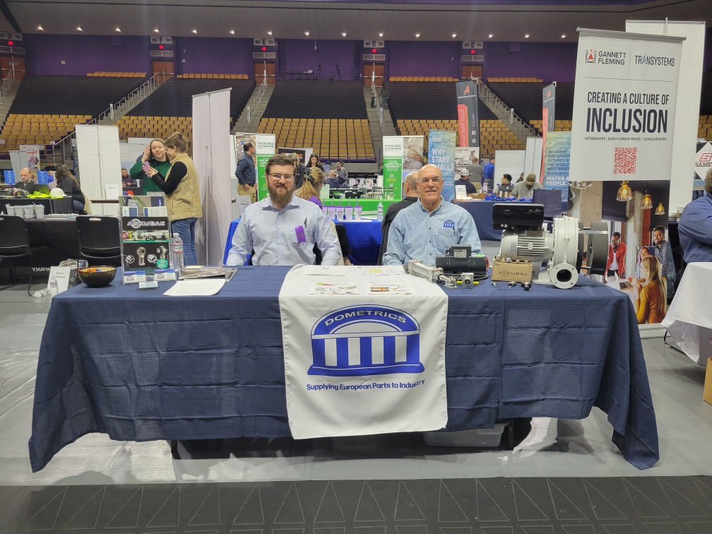 Two men at Dometrics booth during conference showcasing European parts.
