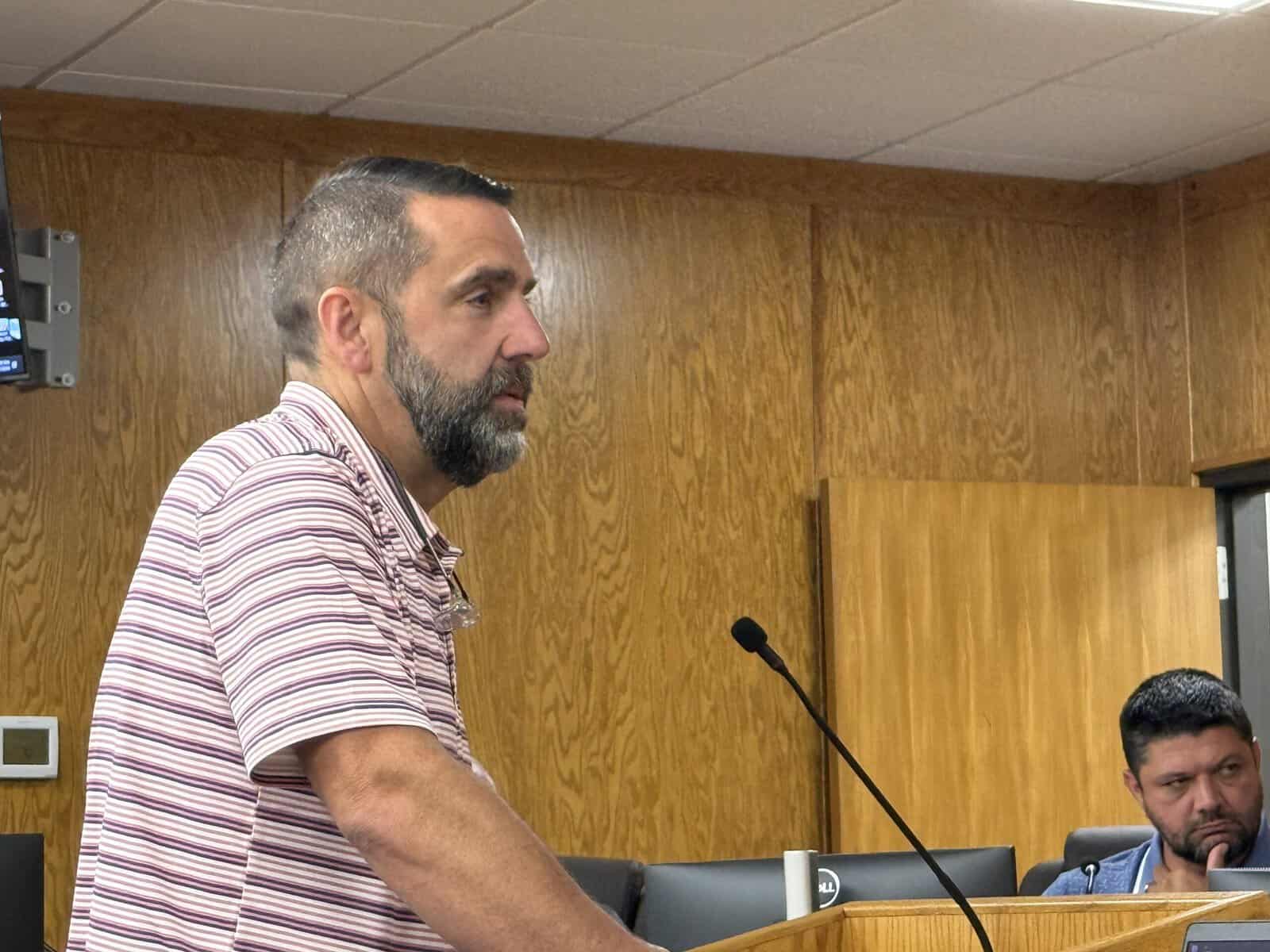 Man speaking into microphone during public meeting on budget and services.