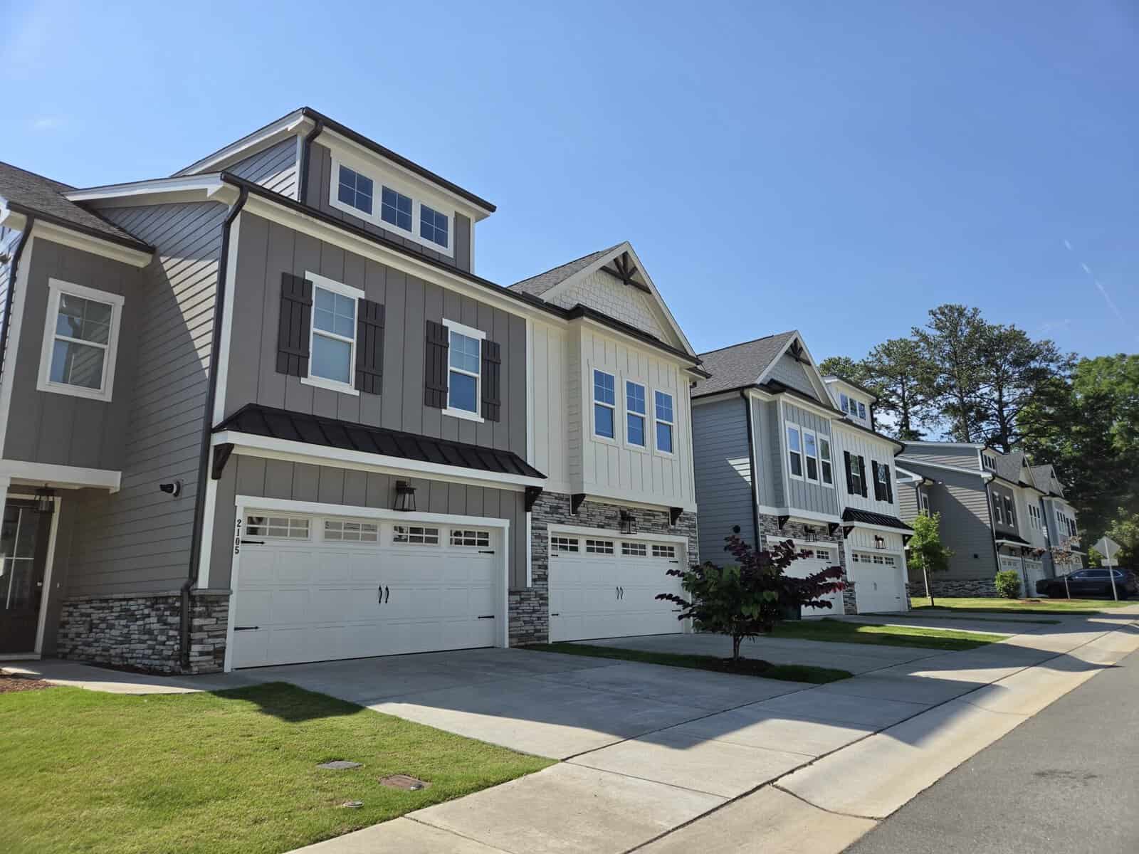 Row of modern townhouses with garages and well-maintained lawns under a clear blue sky.