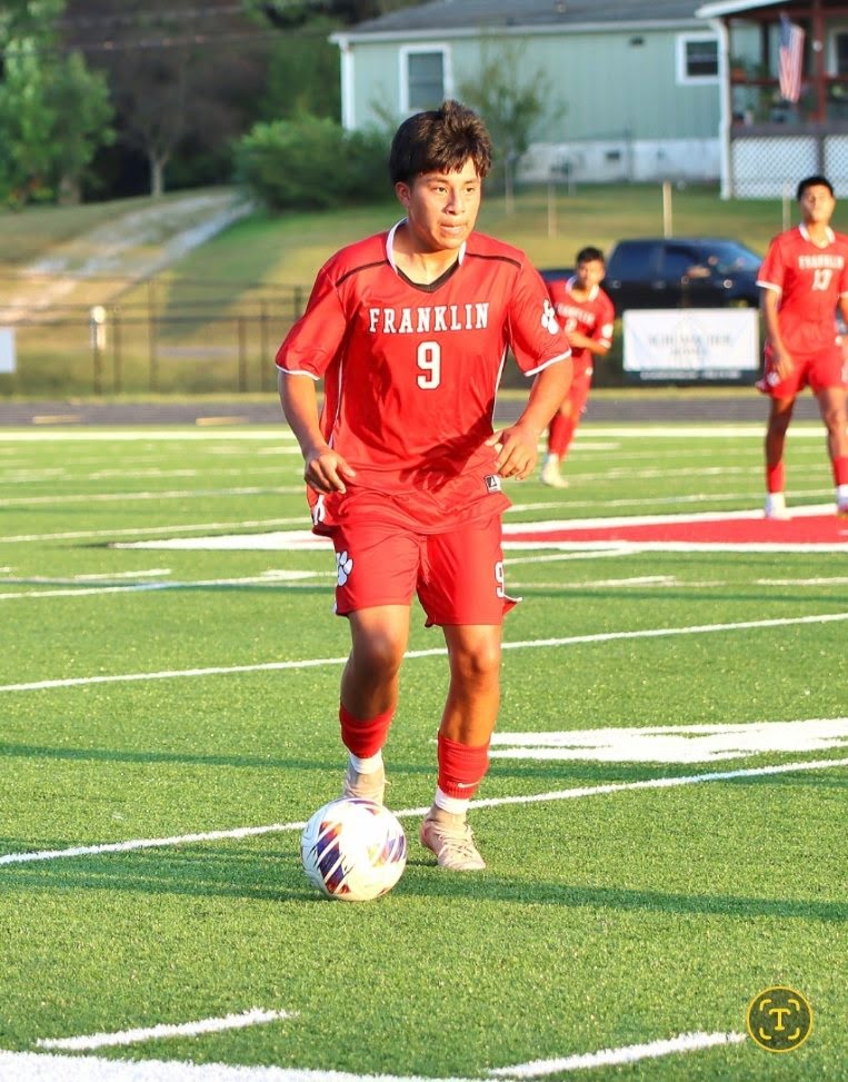 Franklin soccer player in red uniform dribbling ball on field.