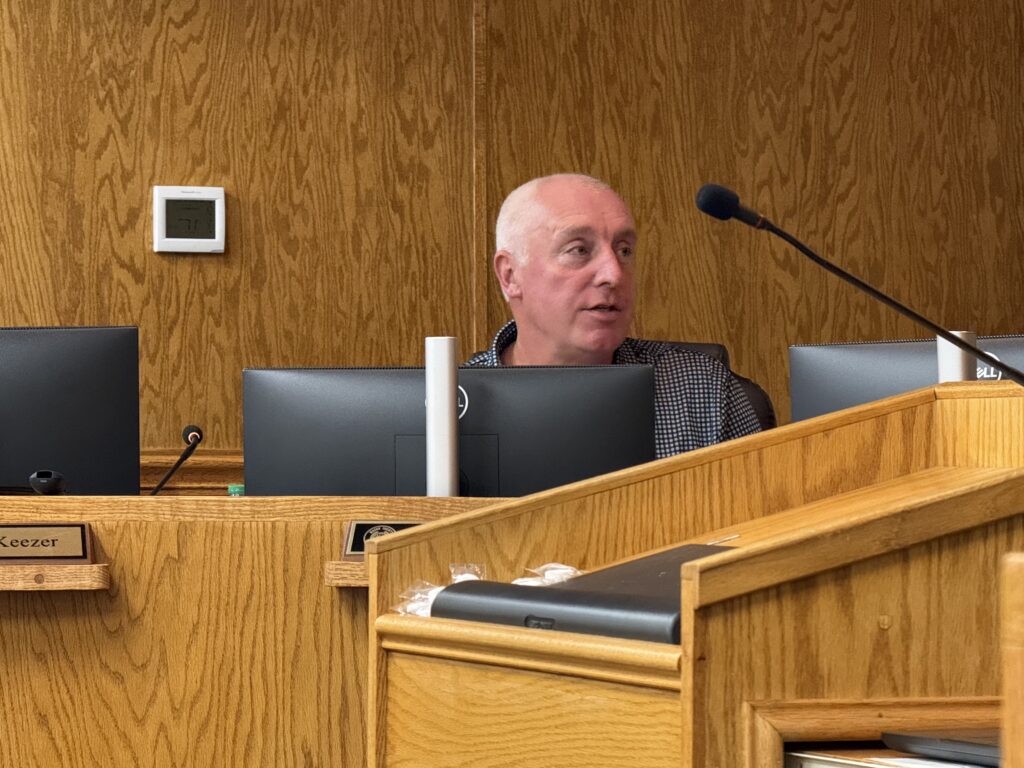 County commissioner speaking at October meeting in wood-paneled room.