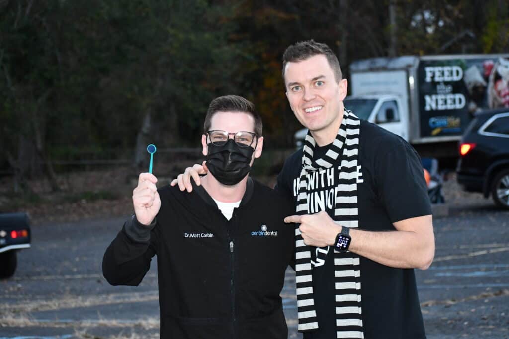 Two men smiling outdoors, one holding a dental tool, in front of a food truck.