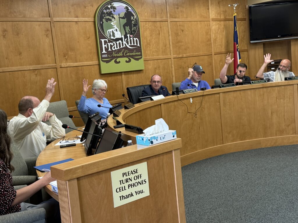 Franklin town council meeting with members raising hands in discussion.