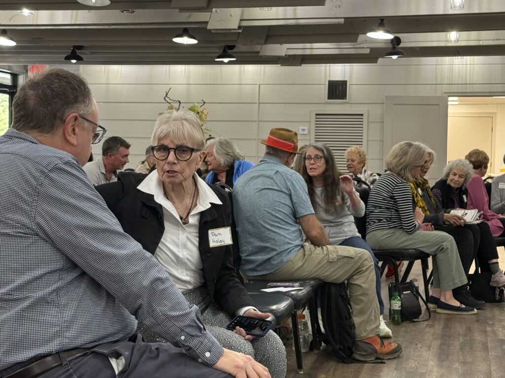 People seated in a discussion circle at an indoor event in Highlands community meeting.