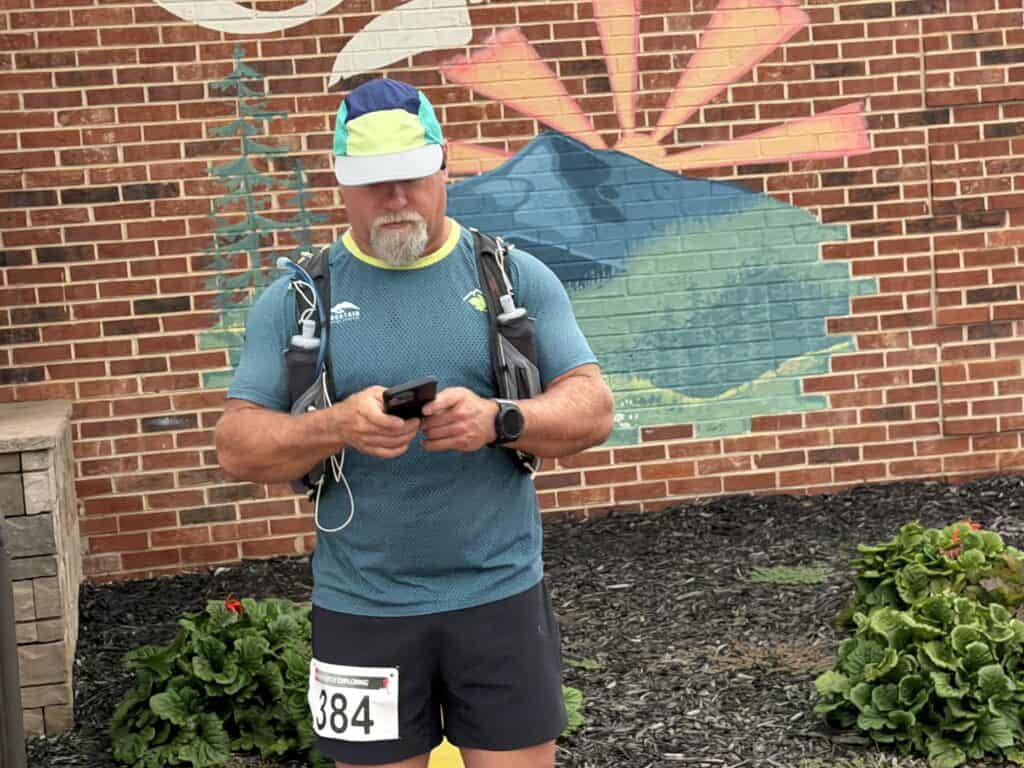 Man with backpack checking phone in front of brick wall with mural.