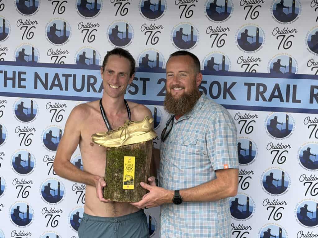 Two men celebrating at Outdoor 76 Trail Run event, holding a trophy.