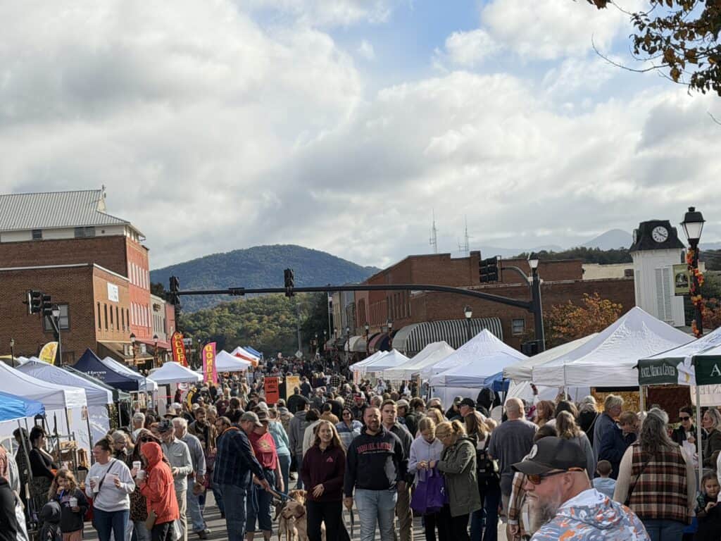 Crowd enjoying fall festival with tents and mountain backdrop in Franklin.